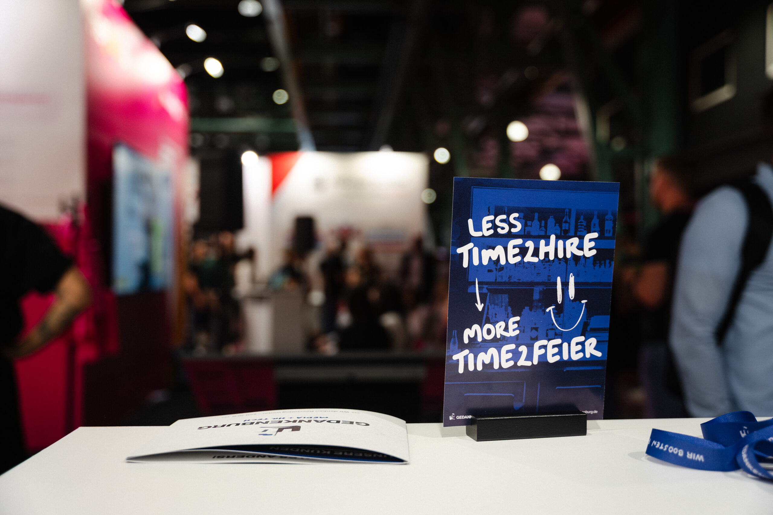 TalentPro Messe München 2025. Messestand Gedankenburg GmbH. Blau Schwarzer Flyer mit weißer Schrift "Less time 2 hire, more time 2 feier".